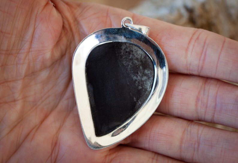 May include: A silver pendant with a dark grey stone set in a heart-shaped frame.