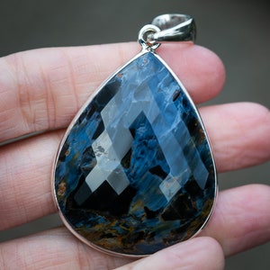 May include: A teardrop-shaped pendant with a blue and gold tiger's eye gemstone set in sterling silver.