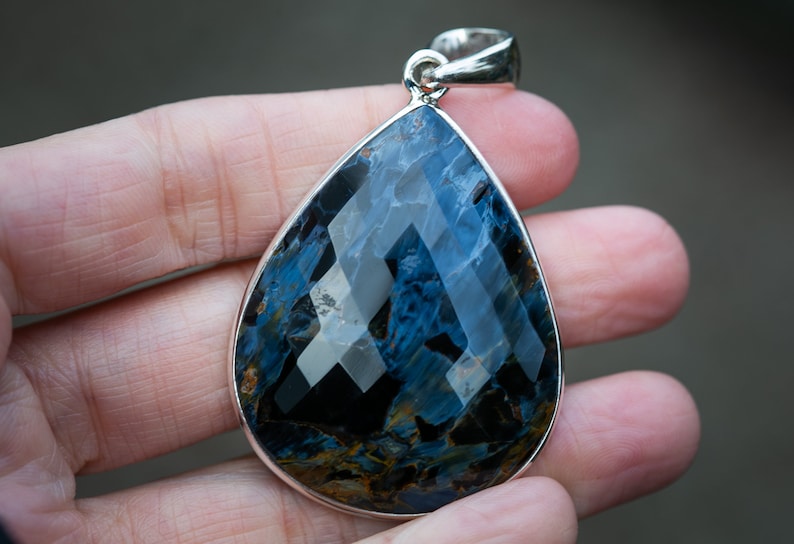 May include: A teardrop-shaped pendant with a blue and gold tiger's eye gemstone set in sterling silver.