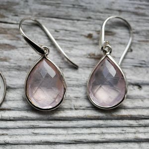 May include: A pair of silver dangle earrings with pink teardrop-shaped gemstones.