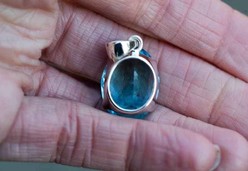 Pu&ograve; includere: Un ciondolo d'argento con una grande pietra preziosa rotonda di colore blu chiaro. Il ciondolo ha un design semplice ed elegante.