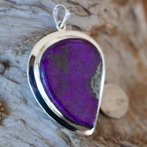 May include: A silver pendant with a large purple and black gemstone. The pendant is shaped like a teardrop and has a smooth, polished finish.