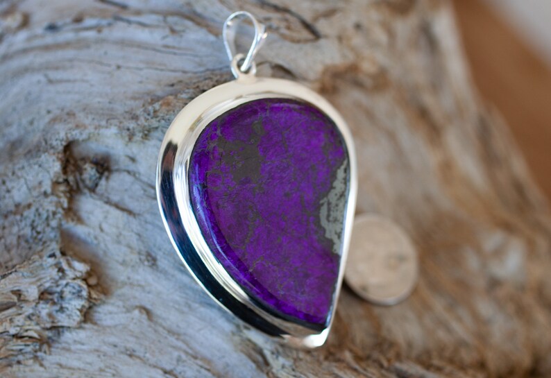 May include: A silver pendant with a large purple and black gemstone. The pendant is shaped like a teardrop and has a smooth, polished finish.