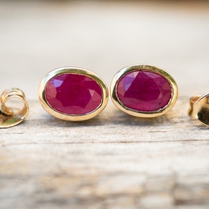 May include: A pair of oval-shaped ruby earrings set in gold. The earrings have a 14K gold hallmark.