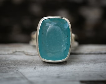 May include: A silver ring with a large, rectangular, light blue gemstone.