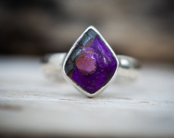 May include: A silver ring with a purple and black gemstone set in a diamond-shaped setting.