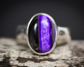 May include: A silver ring with a purple and black oval gemstone. The gemstone has a unique pattern of purple and black.