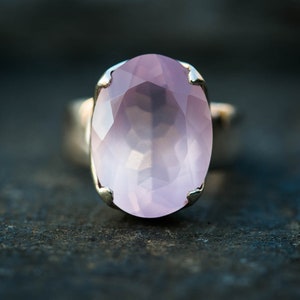 May include: A silver ring with a large, oval-shaped, faceted, light pink gemstone.