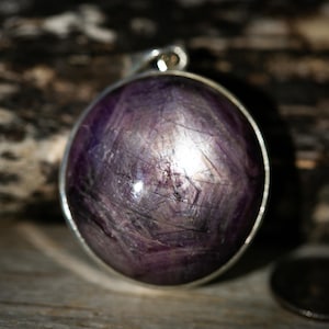 May include: A silver pendant featuring a large, round, purple gemstone with a starburst pattern.