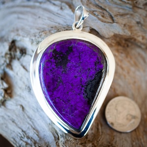 May include: A silver pendant with a large, teardrop-shaped purple and black stone. The stone has a mottled, textured surface.