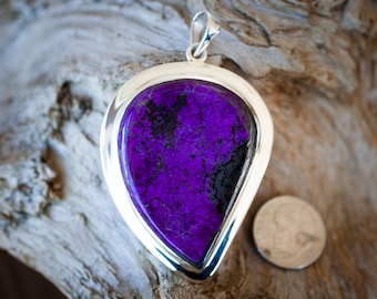 May include: A silver pendant with a large, teardrop-shaped purple and black stone. The stone has a mottled, textured surface.