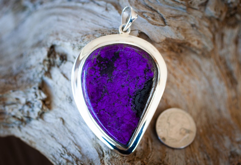May include: A silver pendant with a large, teardrop-shaped purple and black stone. The stone has a mottled, textured surface.