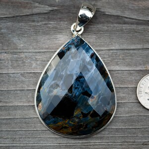 May include: A teardrop-shaped pendant with a blue and gold tiger's eye gemstone set in sterling silver. The pendant is approximately the size of a US dime.