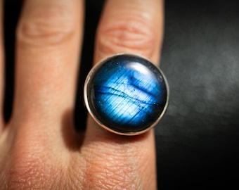 May include: A silver ring with a large, round, blue labradorite gemstone. The stone has a dark blue base with iridescent white and blue streaks.