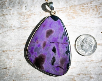 May include: A purple and black gemstone pendant with a silver bail. The pendant is shaped like a teardrop and has a unique, swirling pattern.