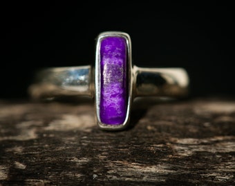 May include: A silver ring with a purple gemstone set in a rectangular shape.