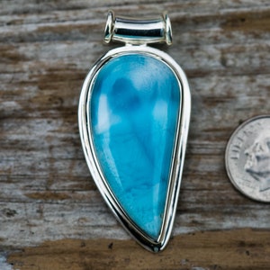 May include: A teardrop-shaped pendant with a blue and white gemstone set in a silver frame. The pendant is about the size of a US dime.