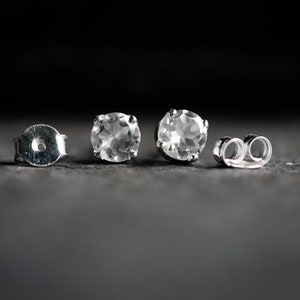 May include: A pair of silver stud earrings with clear round gemstones. The earrings have butterfly backings.