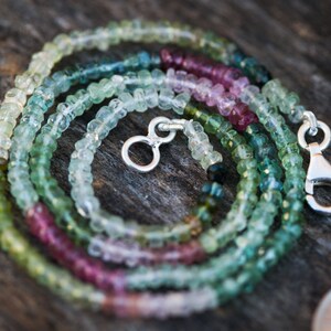 May include: A multi-coloured gemstone necklace with a silver clasp. The necklace is made of small, round beads in shades of green, pink, and white.