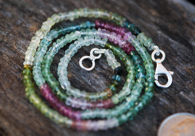 May include: A multi-coloured gemstone necklace with a silver clasp. The necklace is made of small, round beads in shades of green, pink, and white.