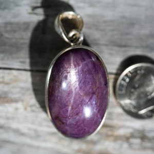 May include: A purple star sapphire pendant set in sterling silver. The pendant is oval shaped and measures approximately 1 inch in length. The star sapphire has a six-rayed star.