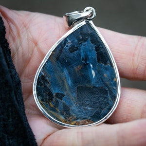 May include: A teardrop-shaped pendant with a blue and gold tiger's eye gemstone set in sterling silver.