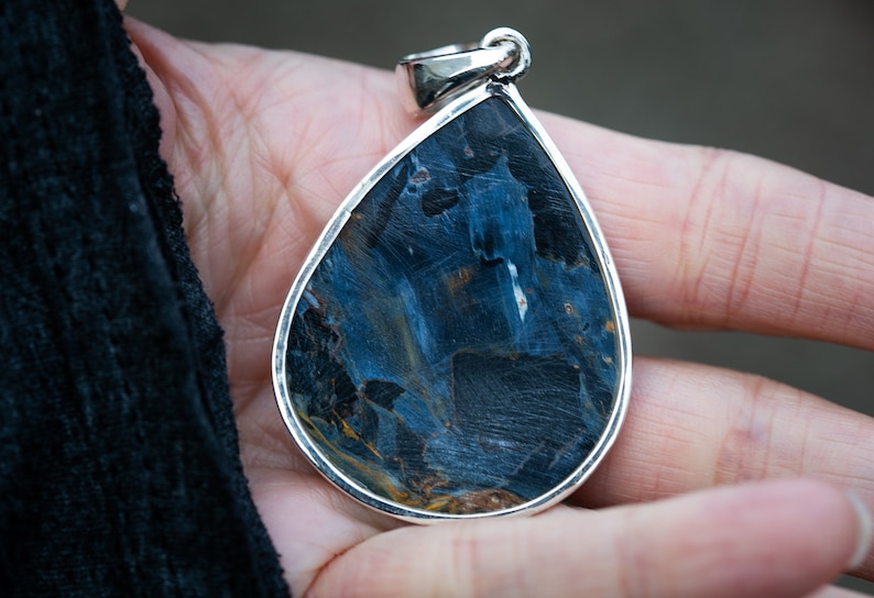 May include: A teardrop-shaped pendant with a blue and gold tiger's eye gemstone set in sterling silver.