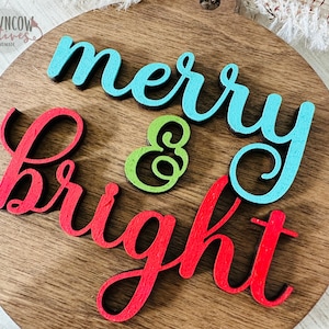 May include: A wooden round sign with the words "merry & bright" in red, blue, and green paint.