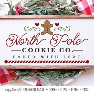 May include: A white sign with a brown wooden frame, featuring a gingerbread man cookie, red hearts, and the text "North Pole - COOKIE CO. - BAKED WITH LOVE".