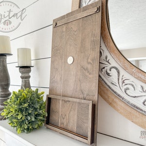 May include: A wooden wall shelf with a built-in phone stand. The shelf is stained a dark brown color and has a rustic look. The phone stand is made of the same wood and is attached to the bottom of the shelf. The shelf is mounted on a white wall.