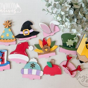 May include: A collection of colorful wooden cutouts in various shapes, including a party hat, witch hat, bunny ears, and a pencil. The cutouts are painted with bright colors and feature holiday-themed designs. The image includes the text "BROWNCOW CREATIVES" and "INSTANT DIGITAL DOWNLOAD".