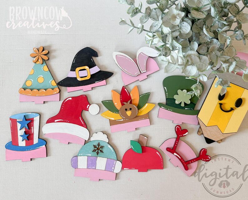 May include: A collection of colorful wooden cutouts in various shapes, including a party hat, witch hat, bunny ears, and a pencil. The cutouts are painted with bright colors and feature holiday-themed designs. The image includes the text "BROWNCOW CREATIVES" and "INSTANT DIGITAL DOWNLOAD".