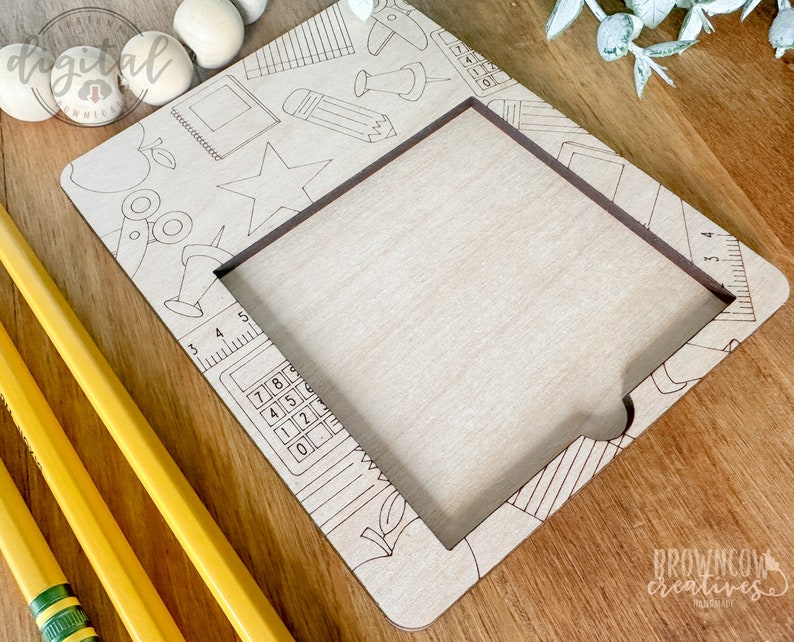 May include: A wooden frame with a cutout for a photo or artwork. The frame is decorated with a school-themed design, including a ruler, a calculator, a pencil, a star, and a scissors. The frame is unfinished and ready to be painted or stained.
