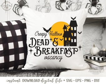 May include: A white cushion with a black and white checked cushion behind it. The cushion has a black and yellow graphic of a haunted house with bats and a moon. The text on the cushion reads "Creepy Hallow Dead & Breakfast vacancy".