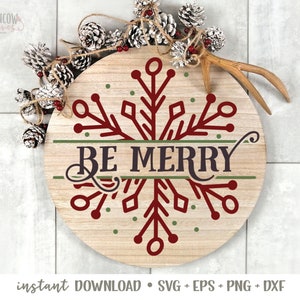 May include: A round wooden sign featuring a red snowflake design and the text "BE MERRY" in a green banner. The sign is surrounded by pine cones and a white tiled background.