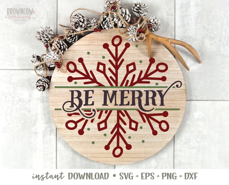 May include: A round wooden sign featuring a red snowflake design and the text "BE MERRY" in a green banner. The sign is surrounded by pine cones and a white tiled background.