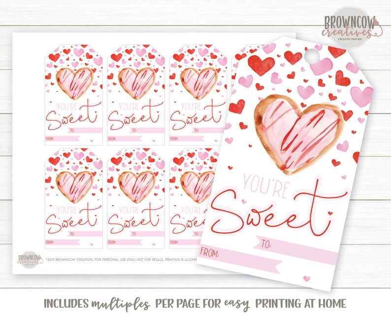 May include: Printable Valentine's Day gift tags featuring a watercolor illustration of a heart-shaped cookie with pink frosting and red sprinkles. The tags have the text "You're Sweet" with spaces for "From" and "To".