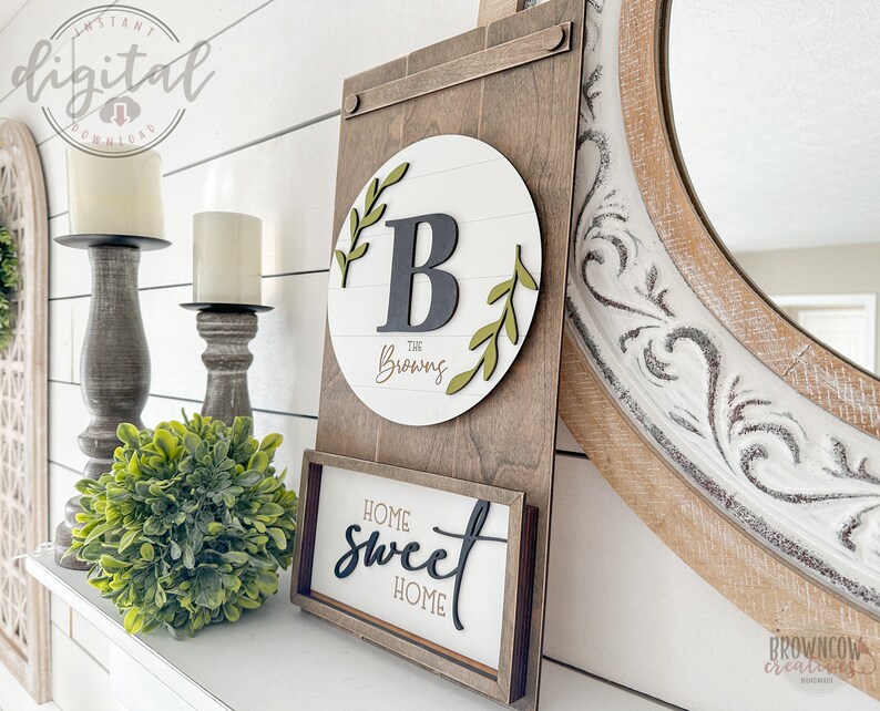 May include: A wooden sign with a white circle and the letter "B" in black with green leaves around it. The text "The Browns" is written in cursive below the letter. A smaller wooden sign below says "Home Sweet Home" in black cursive lettering.