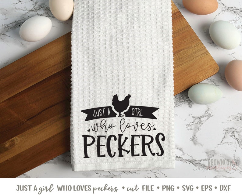 K&ouml;nnte beinhalten: Ein wei&szlig;es K&uuml;chentuch mit schwarzem Text, der "Just a girl who loves peckers" lautet. Eine schwarze Silhouette eines Huhns befindet sich &uuml;ber dem Text. Das Tuch liegt auf einer Holzoberfl&auml;che mit Eiern.