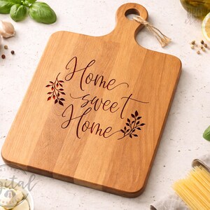 May include: A rectangular wooden cutting board with a handle and the words "Home sweet Home" engraved in a cursive font. The board has a light brown color and is surrounded by ingredients.