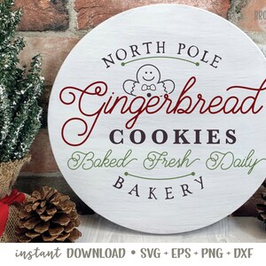 May include: A white round sign with the text "North Pole Gingerbread Cookies Baked Fresh Daily Bakery" in red, green, and black lettering. A gingerbread man cookie illustration is in the center of the sign.