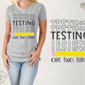 Puede incluir: Una camiseta gris con texto negro que dice "Testing Testing Testing One, Two, Three" y un lápiz amarillo con una goma rosa.