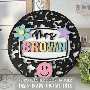 Peut inclure: Porte-manteau en bois découpé au laser noir et blanc avec un fond blanc sur lequel est inscrit "Mrs. BROWN" en lettres arc-en-ciel. Le porte-manteau est orné d'un motif animalier noir et blanc et d'un smiley rose avec un éclair.