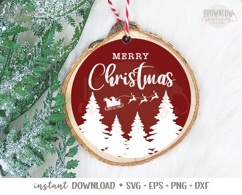 May include: A round wooden bauble with a red background and white text that says "Merry Christmas". The bauble features a silhouette of a sleigh with Santa Claus and reindeer flying over a forest of white pine trees.