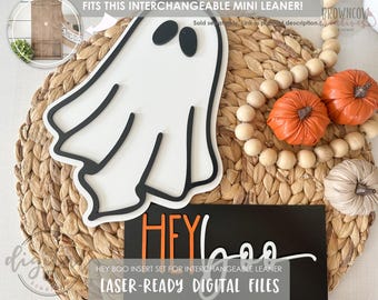 Puede incluir: Una decoración en forma de fantasma blanco con ribetes y ojos negros, combinada con calabazas naranjas y una guirnalda de cuentas de madera. También hay un letrero negro con las palabras "HEY boo" en blanco y naranja. El texto "HEY BOO INSERT SET FOR INTERCHANGEABLE LEANER" es visible.