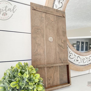 May include: A brown wooden sign with a shelf and a metal hook. The sign is leaning against a white wall.