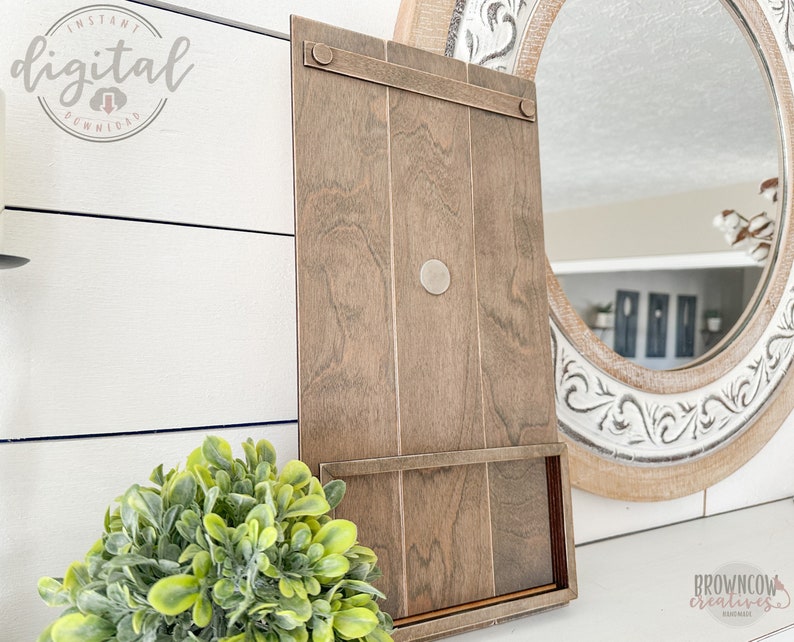 May include: A brown wooden sign with a shelf and a metal hook. The sign is leaning against a white wall.