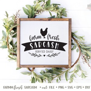 K&ouml;nnte beinhalten: Ein wei&szlig;es Schild mit braunem Holzrahmen, das eine schwarze Silhouette eines Huhns und den Text "farm fresh SARCASM SERVED DAILY" zeigt.