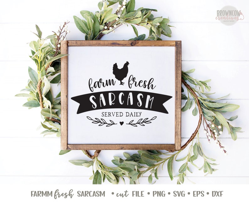 K&ouml;nnte beinhalten: Ein wei&szlig;es Schild mit braunem Holzrahmen, das eine schwarze Silhouette eines Huhns und den Text "farm fresh SARCASM SERVED DAILY" zeigt.