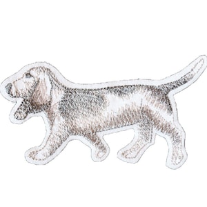 Könnte beinhalten: Ein gestickter Aufnäher mit einem Hund, möglicherweise ein Basset Hound, der mit herausgestreckter Zunge geht. Der Aufnäher ist braun und weiß.
